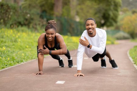 Téléchargez les photos : Heureuse jeune femme afro-américaine et le gars qui fait pousser l'exercice dans le parc extérieur, espace libre. Soins du corps, entraînement en ville ensemble, mode de vie actif et motivation avec le coach - en image libre de droit