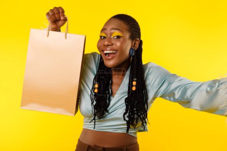 Téléchargez les photos : Shopaholics Choice. Femme cliente noire excitée célébrant les achats réussis tenant son sac en papier Shopper posant pour Selfie debout sur fond jaune studio. Offre commerciale Publicité - en image libre de droit