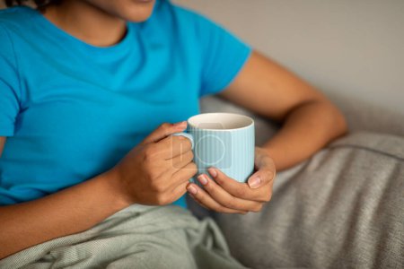 Photo for Ill, tired millennial curly black lady hold cup of tea, enjoy free time on sofa, rest alone with plaid in cozy living room interior, close up. Coffee break in evening, relax and treatment at home - Royalty Free Image