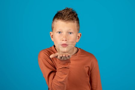 Photo for Funny Little Boy Pouting Lips And Blowing Air Kiss At Camera, Romantic Preteen Male Child Kissing Somebody, Flirty Caucasian Kid Standing Isolated Over Blue Background In Studio, Copy Space - Royalty Free Image