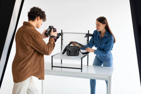 Photo for The art of teamwork. Professional photographer and his assistant doing content photoshoot for female bags, woman helping while working in team in photostudio - Royalty Free Image