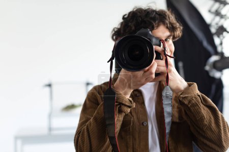 Foto de Fotógrafo masculino tomando fotos con cámara profesional en photostudio, joven trabajando en sesión de fotos, espacio libre. Empleo y ocupaciones - Imagen libre de derechos