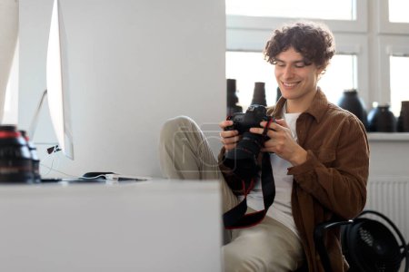 Photo for Modern arts and creative career concept. Happy handsome professional photographer guy holding camera using computer sitting at workplace, free space - Royalty Free Image