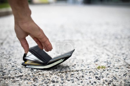 Téléchargez les photos : Vue rapprochée de l'homme noir ramassant portefeuille perdu plein de billets d'argent sur la rue de la ville, foyer sélectif, espace vide. Concept d'argent perdu - en image libre de droit