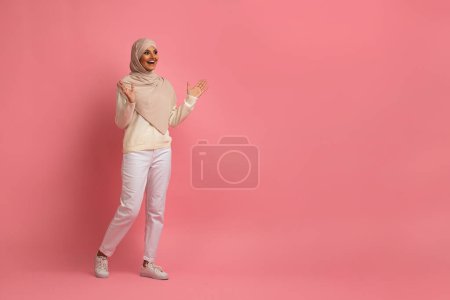 Foto de Gran oferta. Mujer musulmana alegre en Hijab mirando al costado del espacio de copia con emoción, mujer islámica emocional levantando las manos y exclamando Wow, disfrutando de una agradable sorpresa, de pie sobre un fondo rosa - Imagen libre de derechos
