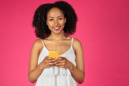 Foto de Retrato de mujer afroamericana milenaria feliz con teléfono, disfrutar del chat en las redes sociales, aislado en el fondo rosa, estudio. Gadget, mensaje de buenas noticias, venta y blog - Imagen libre de derechos