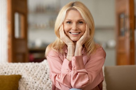 Photo for Ageless Beauty And Anti Aging Skincare. Portrait Of Cheerful Blonde Senior Woman Touching Her Face, Enjoying Soft And Smooth Skin Sitting On Couch At Home, Posing Smiling To Camera - Royalty Free Image