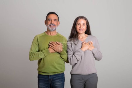 Photo for Happy caucasian elderly man and lady put hands to chest, make gratitude gesture on gray studio background, copy space. Thanks, love, relationships and people emotions, good news - Royalty Free Image