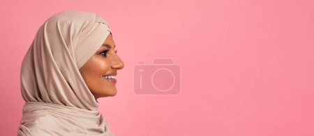 Téléchargez les photos : Profil de femme musulmane souriante en hijab regardant l'espace de copie sur fond rose dans le studio, vue de côté de belle dame islamique heureuse en foulard, bannière pour votre annonce, panorama - en image libre de droit