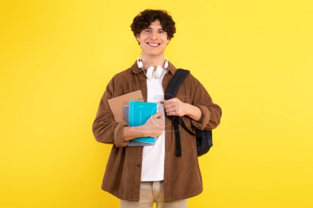 Photo for Academic Enthusiasm. Shot Of Smiling Student Guy Eager To Learn Successfully, Standing With Backpack And Textbooks Ready For University Study, Posing Over Yellow Studio Background - Royalty Free Image