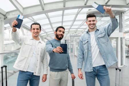 Photo for Vacation Mode. Three Happy Friends Men Ready For Flight, Posing With Luggage Showing Their Passports And Boarding Passes Smiling To Camera, Advertising Tickets Offer In Airport. Time To Travel - Royalty Free Image