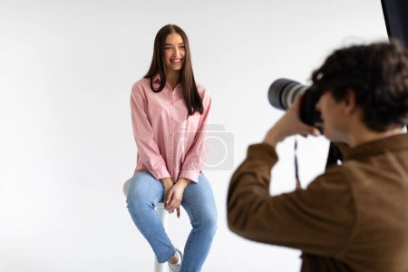 Photo for Creating captivating portraits. Photographer taking photos of young european lady in casual wear, having photoshoot on white background in modern studio - Royalty Free Image