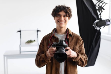 Photo for Professional photographer man holding photocamera posing smiling to camera standing in photostudio while making content photoshoot. Guy taking photos posing with camera - Royalty Free Image