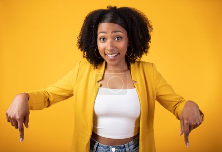 Photo for Happy young black lady showing thumbs down to empty space, isolated on yellow background, studio shot. Sale recommendation and advice, lifestyle, ad and offer, facial expression - Royalty Free Image