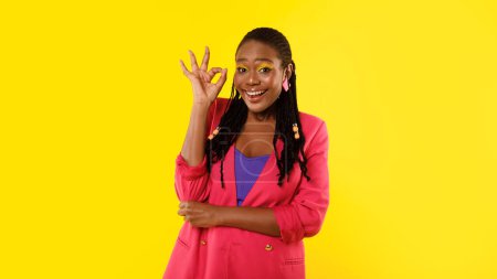Téléchargez les photos : Approbation de style. Femme Afro-Américaine Positive Gesturant Ok debout sur fond jaune studio, portant des vêtements lumineux et du maquillage. Portrait de dame montrant OK Symbole. Panorama - en image libre de droit