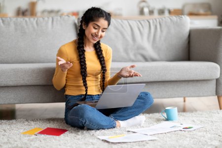 Photo for Teleconference Concept. Happy Young Indian Female Freelancer Making Video Call With Laptop At Home, Smiling Eastern Woman Sitting On Floor, Talking At Web Camera, Enjoying Online Communication - Royalty Free Image