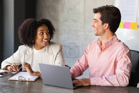 Photo for Happy multiracial coworkers management team young beautiful black lady and european man sitting at table, have conversation during work meeting morning briefing, using laptop. Teamwork concept - Royalty Free Image