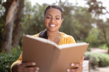 Photo for Happy brazilian student lady reading textbook, studying for exam outdoors, sitting in college campus or park, closeup. Smiling female preparing for school test - Royalty Free Image