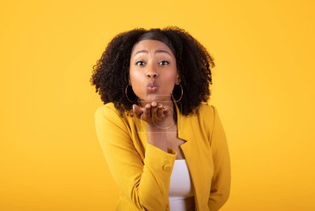 Photo for Pretty flirting black lady blowing air kiss posing at camera over yellow studio background. Love and romance, female playful gesture concept - Royalty Free Image