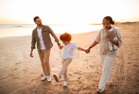 Photo for Salty air, family fair. Happy family walking with their children on vacation on the beach by seaside, parents enjoying evening time with kids outdoors - Royalty Free Image