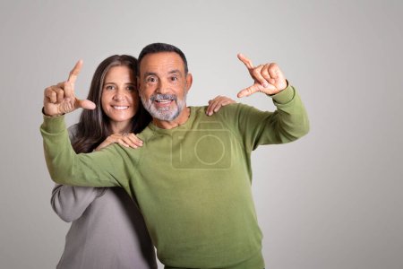 Téléchargez les photos : Vieux couple européen joyeux s'amuser, faire cadre, geste de lentille avec les mains avec de l'espace libre sur fond de studio gris. Art, créativité, publicité et offre, conseils d'experts et mode de vie - en image libre de droit