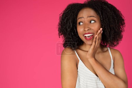 Foto de Feliz sonrisa sorprendida joven mujer rizada negro mirando espacio vacío aislado sobre fondo rosa, estudio. Venta, estilo de vida positivo, buenas noticias, anuncio y oferta, moda, cuidado de belleza - Imagen libre de derechos