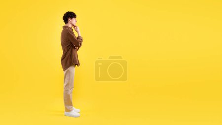 Photo for Let Me Think. Thoughtful Guy Thinking Looking Aside At Empty Space And Touching Chin Posing Over Yellow Studio Background. Side View Shot Of Pensive Young Man. Full Length, Panorama - Royalty Free Image