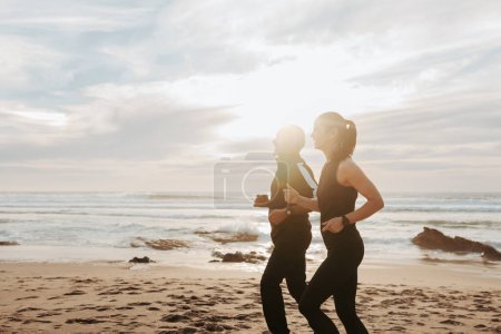 Téléchargez les photos : Heureux homme et femme caucasien mature en vêtements de sport courir le matin sur la plage de la mer, en plein air, profil. Cardio-training, couple profiter de l'entraînement ensemble, les soins de santé, les soins du corps en été - en image libre de droit
