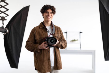 Photo for Studio stories. Positive guy in stylish casual outfit holding digital camera and smiling, professional photographer enjoying his job at photo studio, copy space - Royalty Free Image
