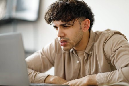 Photo for Portrait Of Tired Young Man Using Laptop Computer, Squinting Eyes Looking At Screen Having Problems With Vision Working Online Sitting At Desk In Office. Side View, Selective Focus - Royalty Free Image