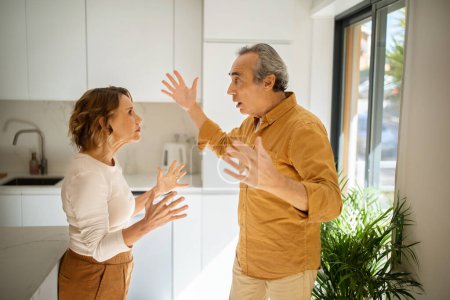 Photo for Relationship problems. Angry senior man arguing with his wife at kitchen, mad spouses shouting at each other and gesturing, having difficulties in marriage, side view - Royalty Free Image