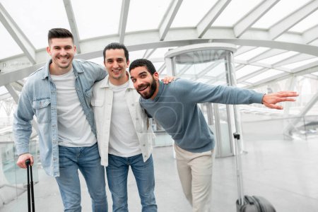 Photo for Travel Companions. Group Of Friends Guys Posing With Their Suitcases Embracing Smiling To Camera, Sharing Vacation Trip Moments In Airport Departure Terminal Indoors. Joy Of Globetrotting Concept - Royalty Free Image