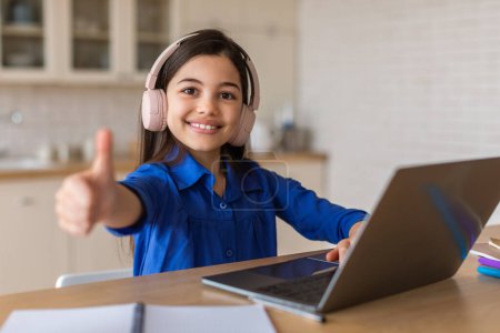 Photo for I Like E-Learning. Smiling Schoolgirl Using Laptop Computer And Gesturing Thumbs Up Approving Online Lecture Learning At Home. School Kid Girl Advertising Online Education Offer. Selective Focus - Royalty Free Image