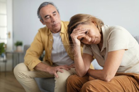 Photo for Couple misunderstanding. Depressed senior wife sitting upset after argue with husband, woman touching head, tired of domestic conflicts with spouse - Royalty Free Image