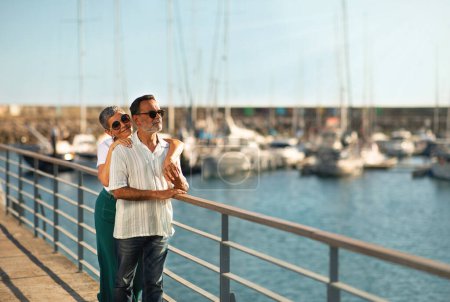 Téléchargez les photos : Concept de vacances d'été. Aimer couple de personnes âgées embrasser à Marina Pier à la recherche de yachts de luxe et voiliers, profiter de la journée ensoleillée au bord de la mer en plein air. Espace vide pour le texte - en image libre de droit