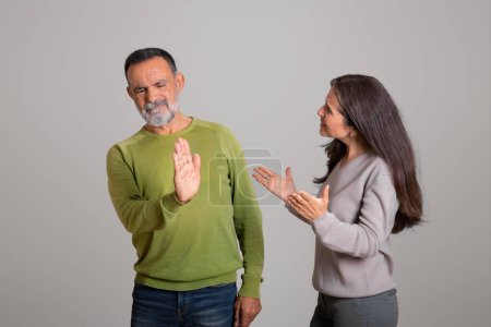 Photo for Aggressive angry caucasian aged wife scolds husband, man makes stop sign, isolated on gray background, studio. Emotions from quarrel, scandal at home, relationship problems and stress - Royalty Free Image