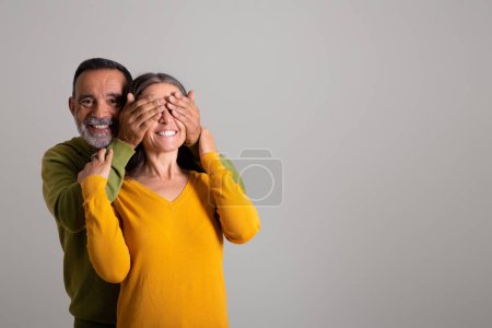Photo for Cheerful old european husband closes eyes to his wife, make surprise on gray studio background. Ad and offer, sale and lifestyle, celebrate holiday together, lifestyle, date - Royalty Free Image