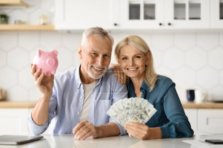 Photo for Investments Concept. Smiling Senior Couple Holding Piggybank And Dollar Cash In Hands At Home, Happy Elderly Spouses Saving Money, Advertising Private Pension Plan, Posing In Kitchen Interior - Royalty Free Image