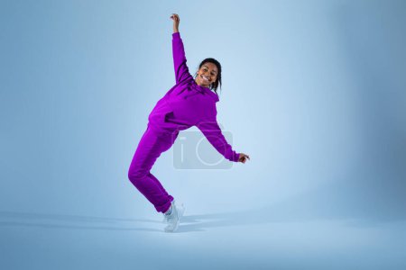 Photo for Happy african american woman in bright sportswear enjoying dancing and expressing emotions, posing on blue background, copy space. Concept of dance, dynamics, movement and action - Royalty Free Image