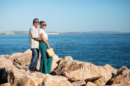 Téléchargez les photos : Vacances de rêve. Happy European Senior Couple Hugging Near Ocean Posing Porter des lunettes de soleil à l'extérieur. Conjoints Profitant des années d'or voyageant ensemble au bord de la mer. Longueur totale, Espace de copie - en image libre de droit