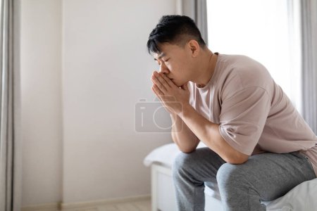 Photo for Side view of frustrated handsome middle aged asian man in pajamas sitting alone on bed at home, experiencing difficulties in relationships, marital conflict, separation, loss of oved one, copy space - Royalty Free Image