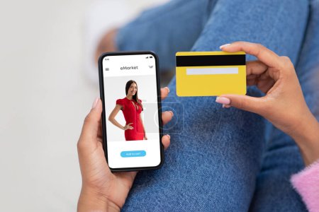 Photo for Millennial black woman using modern phone with fashion store on screen and credit card, paying for order and services online, cropped, close up. Customer buy clothes at app, website - Royalty Free Image