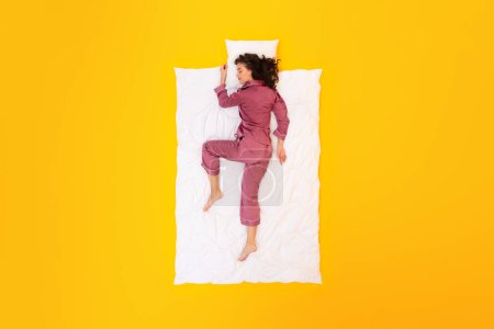 Photo for Serenity Sleep. Full Length Shot Of Woman Napping in Comfortable Pajamas Sleepwear Over Yellow Studio Background. Peaceful Lady Resting And Sleeping Lying On Pillow and Blanket, Top View - Royalty Free Image