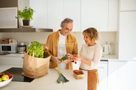Téléchargez les photos : Épouses mariées âgées déballer sac en papier du supermarché, prendre des légumes du sac d'épicerie, famille âgée heureuse profiter du temps ensemble dans l'intérieur de la cuisine - en image libre de droit