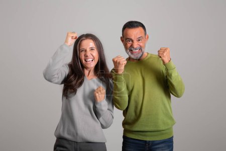 Happy caucasian aged husband and wife celebrating victory, making success gesture, isolated on gray background, studio. Emotions from great news and lifestyle, relationship and win, ad and offer