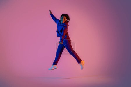 Téléchargez les photos : Portrait complet de femme noire excitée en tenue de sport sautant sur fond néon rose, espace libre. Jeunesse, émotions, mouvement, action, annonce - en image libre de droit