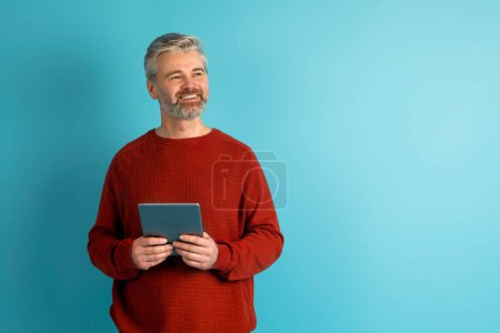 Photo for Stock Trading, Financial Planning Online. Happy middle aged man in casual reviewing his investments or managing his finances on mobile app, using digital tablet on blue studio background, copy space - Royalty Free Image