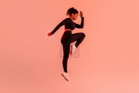 Photo for Dynamic moves. Determined black lady exercising, doing elbow to knee crunches or jumping on red neon studio background, full length, side view - Royalty Free Image