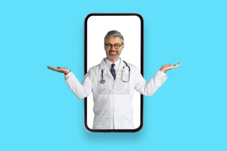 Photo for Digital Health Solutions. Friendly cheerful handsome grey-haired mature doctor in huge cell phone screen gesturing, holding hands like scales, blue studio background, copy space, collage - Royalty Free Image