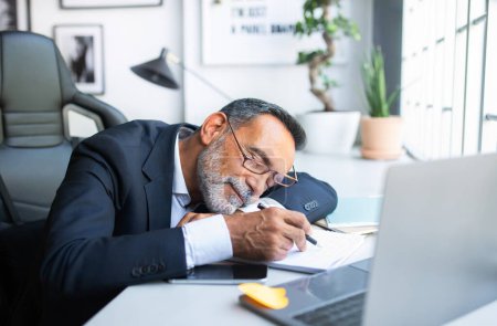 Téléchargez les photos : Fatigué ennuyeux épuisé paresseux vieil homme caucasien en costume au repos, dormir à table à l'intérieur du bureau. Pause, surcharge de travail, stress au travail moderne, entreprise à distance, délai au travail - en image libre de droit